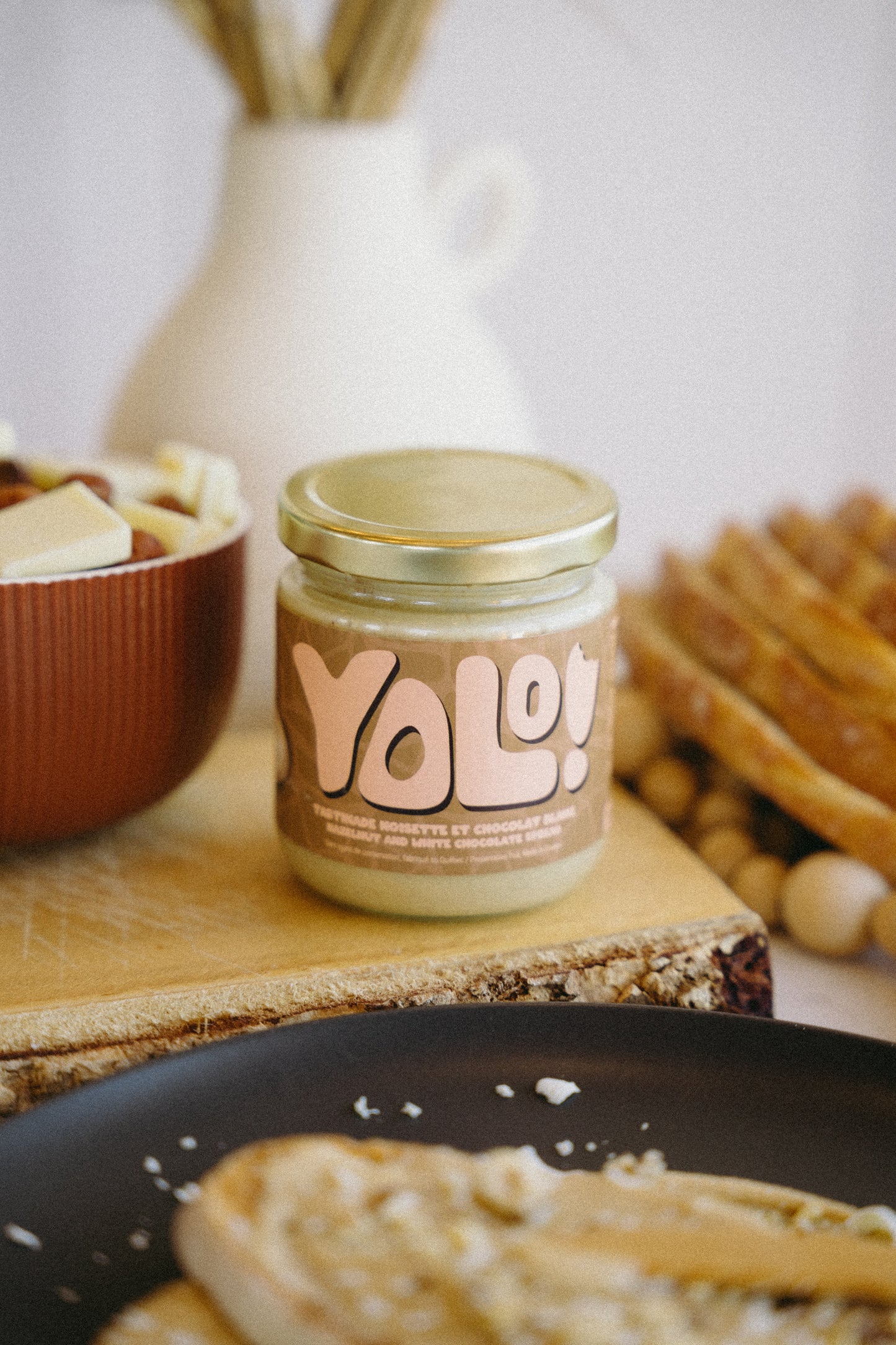 pot de Tartinade de noisette chocolat blanc  avec en arrière pan du chocolat blanc et noisettes dans un bol et des roties et des tranches de pain