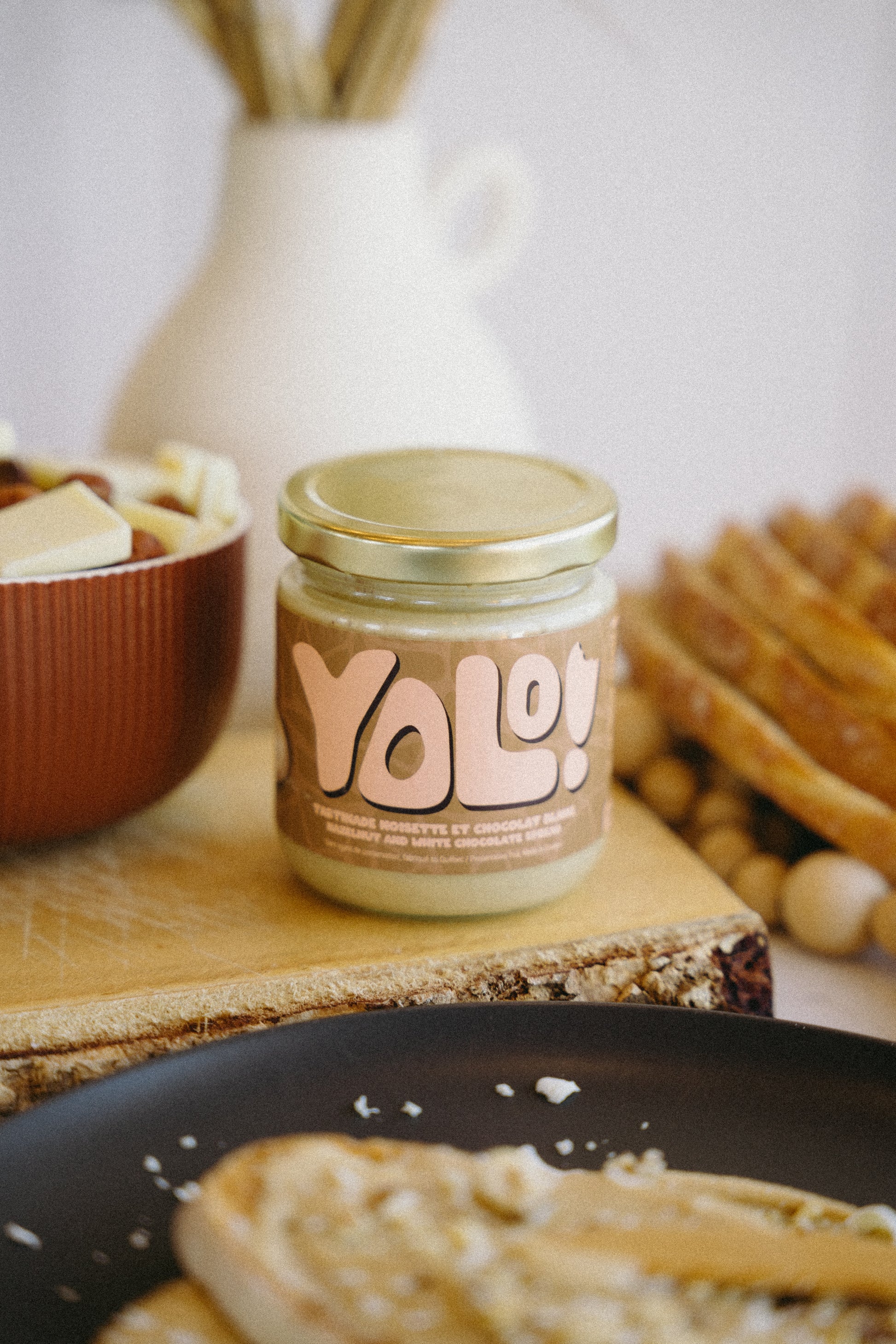pot de Tartinade de noisette chocolat blanc  avec en arrière pan du chocolat blanc et noisettes dans un bol et des roties et des tranches de pain
