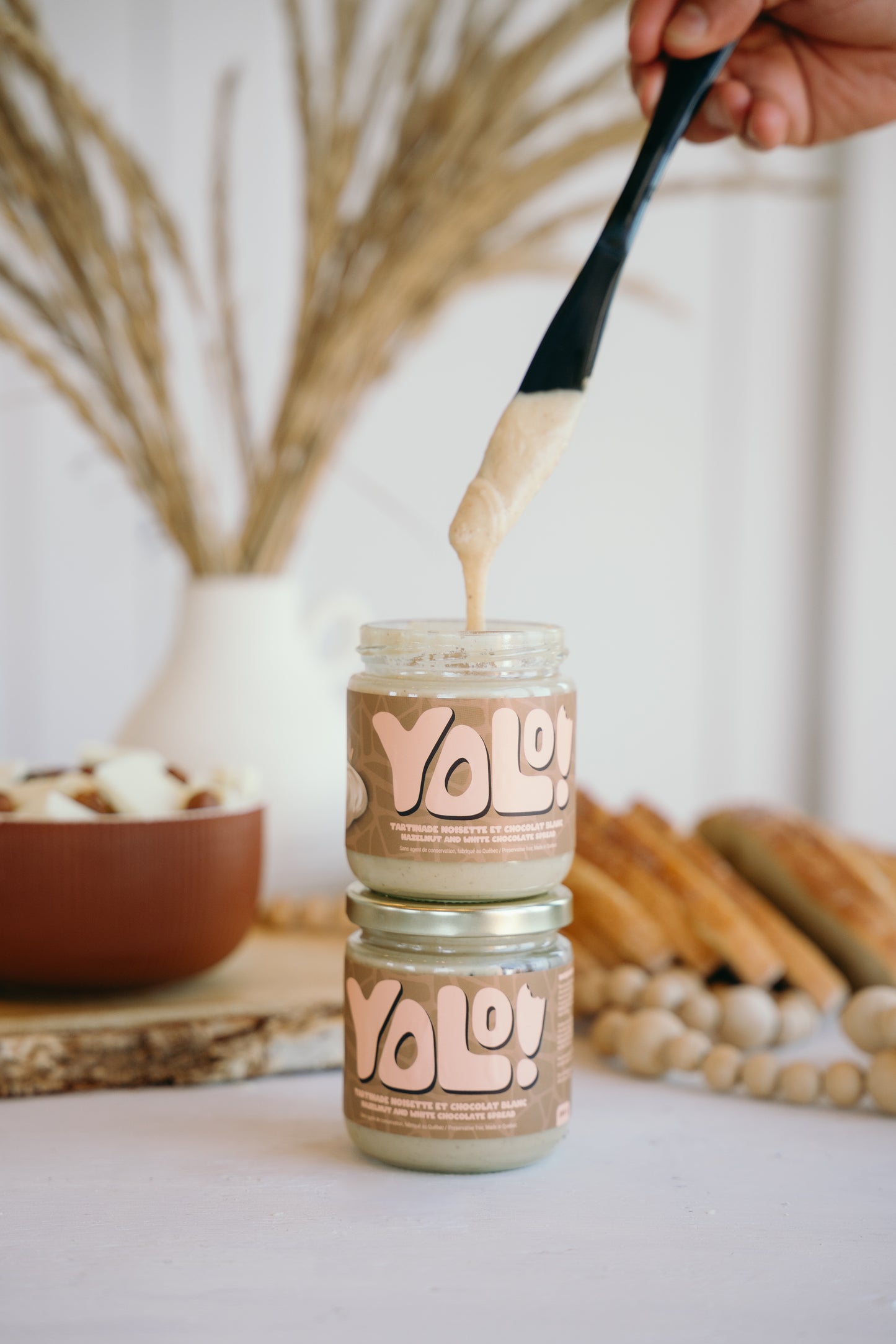 2 pots un par dessus l'autre de Tartinade de noisette chocolat blanc  avec un couteau noir qui pige de la tartinade das un des pots. 