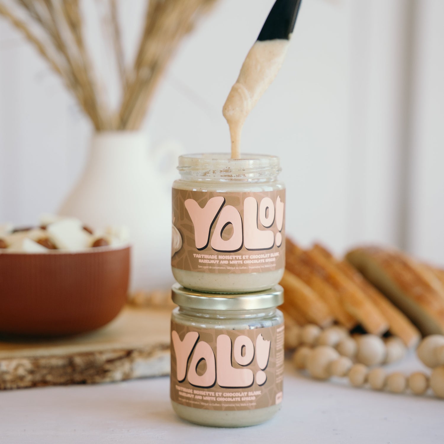 2 pots un par dessus l'autre de Tartinade de noisette chocolat blanc  avec un couteau noir qui pige de la tartinade das un des pots. 